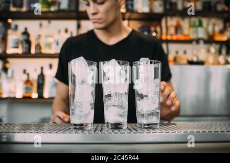 Giovane uomo che indossa abiti neri in piedi dietro il bancone bar, preparando bevande. Foto Stock