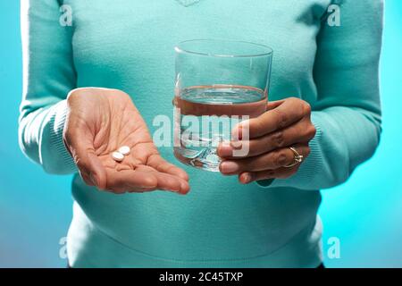 Primo piano di donne che tengono compresse e bicchiere d'acqua, su sfondo blu. Foto Stock