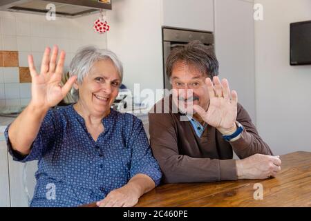 Uomo anziano e donna che sventolano alla macchina fotografica, celebrazione online durante il blocco di Coronavirus. Foto Stock