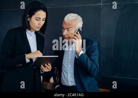 Imprenditore e la donna che guarda la tavoletta digitale e rendere lo smartphone nella chiamata boardroom Foto Stock