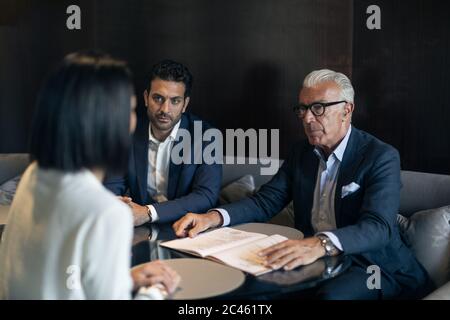 Due imprenditori seduti in hotel Tavolo riunione con imprenditrice Foto Stock