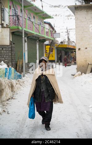 KAZA, SPTI, INDIA - 14 dicembre 2019: Una Vecchia Signora che cammina nel mezzo di una neve nelle strade di Kaza, Valle degli Spiti, in Himachal Pradesh Foto Stock