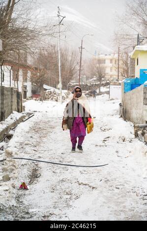 KAZA, SPTI, INDIA - 14 dicembre 2019: Una Vecchia Signora che parla al telefono e cammina nel mezzo di una neve nelle strade di Kaza, nella Valle degli Spiti ad Hima Foto Stock