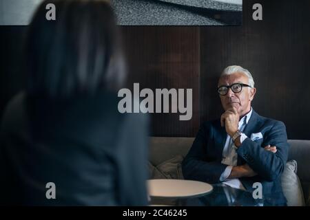 Imprenditore Senior seduti in hotel Tavolo riunione con imprenditrice, sulla spalla vista Foto Stock