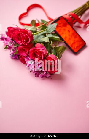 Bouquet di rose rosa con arco a forma di hart e telefono cellulare con schermo di copia Foto Stock