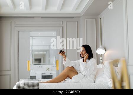 Donna che utilizza smartphone e telecomando in suite Foto Stock