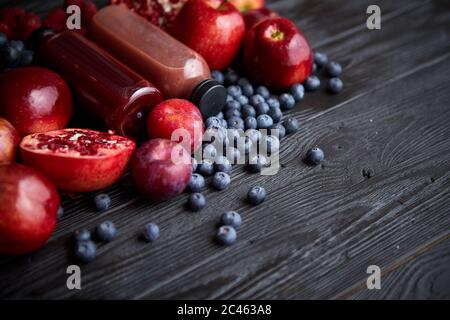 Vari frutti di colore rosso, viola e nero. Mix di frutta e succhi di frutta in bottiglia su nero Foto Stock