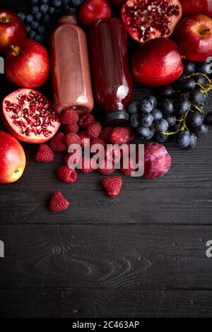 Vari frutti di colore rosso, viola e nero. Mix di frutta e succhi di frutta in bottiglia su nero Foto Stock