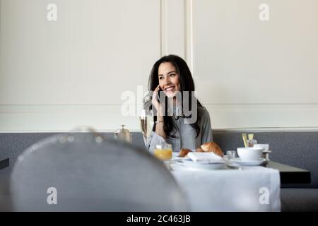 Giovane donna parlando sullo smartphone pur avendo prima colazione con champagne a boutique Hotel in Italia Foto Stock