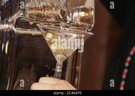 Primo piano di un barman che versa martini in un cocktail vetro guarnito con olive verdi Foto Stock