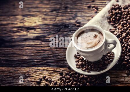 Caffè nero in tazza di porcellana con fagioli sparsi su tavolo rustico in legno Foto Stock