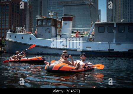 La gente naviga in gommoni nei Docklands di Londra, di fronte allo skyline di Canary Wharf, durante ufficialmente il giorno più caldo dell'anno finora. Foto Stock