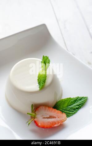 Panna cotta alla menta con fragole, servita in piatto bianco su sfondo bianco di legno Foto Stock