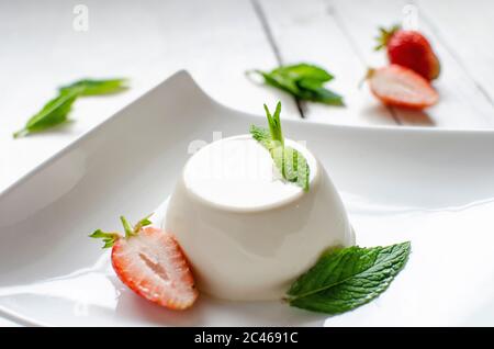 Panna cotta alla menta con fragole, servita in piatto bianco su sfondo bianco di legno Foto Stock