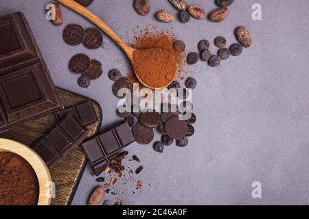 Pezzi e gocce di cioccolato, chicchi di cacao e polvere su sfondo grigio, vista dall'alto Foto Stock