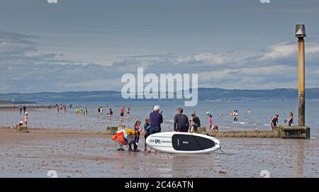 Portobello, Edimburgo, Scozia, Regno Unito. 24 giugno 2020. Il caldo tempo ha portato le famiglie fuori ma il mare non era troppo occupato, molto spazio per mantenere una distanza sociale sulla spiaggia e sul lungomare. Persone su varie tavole da paddle e gonfiabili. Foto Stock