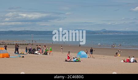 Portobello, Edimburgo, Scozia, Regno Unito. 24 giugno 2020. Il caldo tempo ha portato le famiglie fuori ma il mare non era troppo occupato, molto spazio per mantenere una distanza sociale sulla spiaggia e sul lungomare. Persone su varie tavole da paddle e gonfiabili. Foto Stock