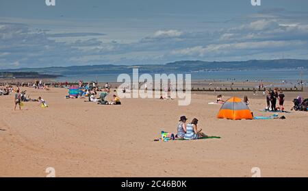 Portobello, Edimburgo, Scozia, Regno Unito. 24 giugno 2020. Il caldo tempo ha portato le famiglie fuori ma il mare non era troppo occupato, molto spazio per mantenere una distanza sociale sulla spiaggia e sul lungomare. Persone su varie tavole da paddle e gonfiabili. Foto Stock