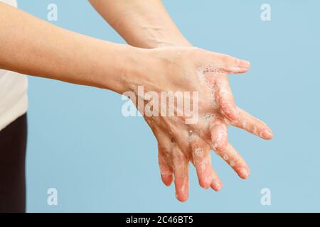 Donna lavando le mani con sapone su sfondo blu. La pulizia corretta delle mani protegge dalle infezioni. Concetto di igiene e pulizia. Foto Stock