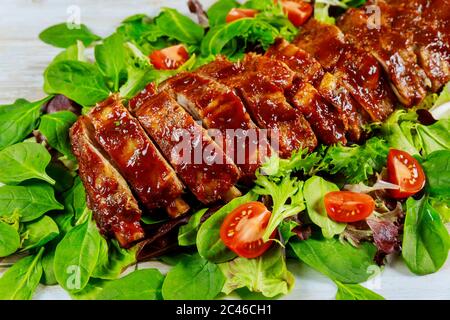 Deliziose costolette di maiale con pomodoro, insalata verde e salsa alla griglia. Foto Stock