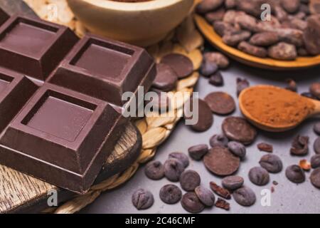 Pezzi e gocce di cioccolato, cacao in grani e polvere su sfondo grigio Foto Stock