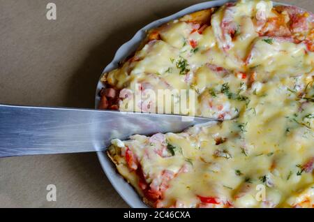 Il coltello da cucina taglia deliziosa pizza con pomodori, salumi e formaggi. Primo piano di pizza appena cotta. Vista dall'alto ad angolo. Messa a fuoco selettiva. Foto Stock