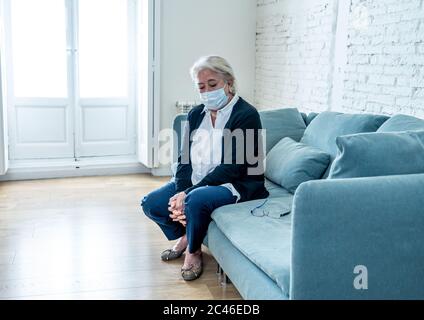 Donna vedova anziana depressa solitaria con maschera protettiva che grida sul divano isolato a casa, triste e preoccupato marito e famiglia scomparso in COVID-19 deat Foto Stock