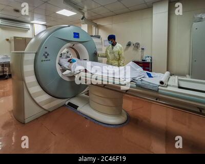 Macchina per tomografia computerizzata (CT) nel reparto di radiologia con tecnico di radiologia che indossa dispositivi di protezione individuale per la preparazione del paziente COVID-19 Foto Stock