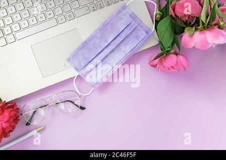 Composizione piatta con maschera medica laptop, caffè, notebook su sfondo rosa. Foto Stock