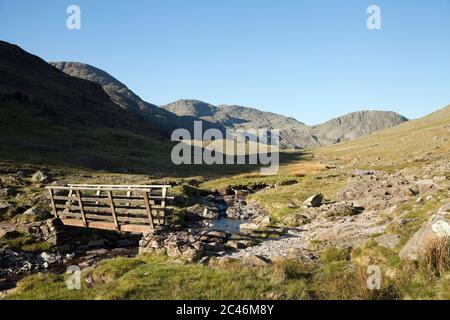 Il massiccio Scafell dalla passerella in legno su Styhead Gill, nel Lake District inglese Foto Stock