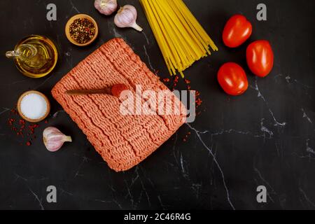 Spaghetti, pomodoro, olio d'oliva, aglio, manzo macinato su sfondo nero vista dall'alto Foto Stock