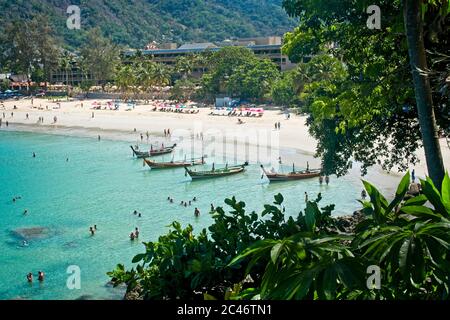 Vista dall'alto che si affaccia sulle barche da pesca locali sulla spiaggia ormeggiato sulla spiaggia di fronte al mare persone sulla spiaggia incorniciato da piante e alberi locali Foto Stock