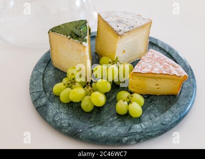 Cheeseboard con aglio Yarg, Gorwydd Caerphilly e Gubbed Irish con uve verdi su banco da cucina bianco Foto Stock