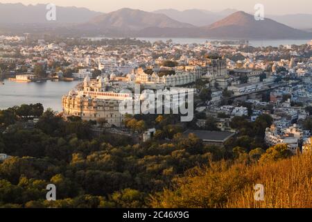 Vista aerea del Palazzo della Città e del Lago Pichola a Udaipur dal punto di osservazione di alta montagna al tramonto, con tonalità calde dell'ora d'oro. Rajasthan, India Foto Stock