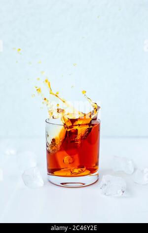 Una foto di un cocktail splash, rocce vetro, cubetti di ghiaccio intorno, sfondo azzurro chiaro, luce naturale Foto Stock