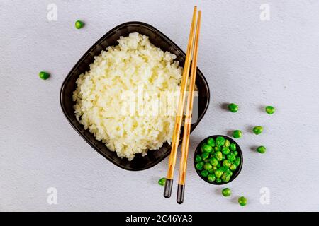 Riso semplice cotto al vapore in una ciotola nera con bastoncini di riso su sfondo bianco. Foto Stock