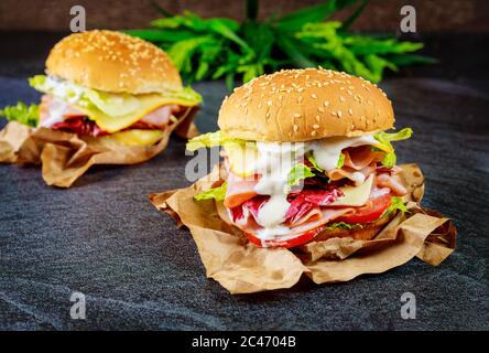 Due panini freschi con prosciutto, formaggio, pomodori, lattuga su fondo scuro. Foto Stock