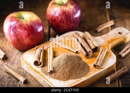 cannella in polvere, macinata e sbucciata. Cannella in una cucina rustica, con mele rosse sullo sfondo. Foto Stock