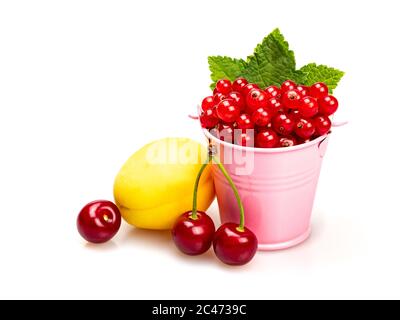 Ribes rosso maturo con foglie verdi in un secchio rosa su sfondo bianco. Vicino albicocca e ciliegie. Foto Stock
