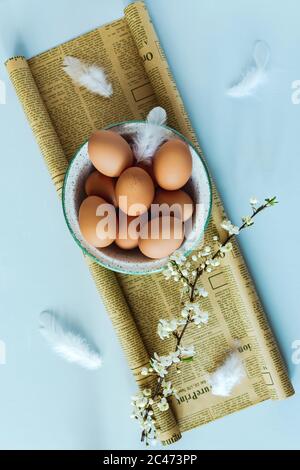 Una Pasqua ancora vita piatta Lay foto di una ciotola di uova marroni su carta artigianale, un ramo fiorente. Sfondo azzurro, vista dall'alto Foto Stock