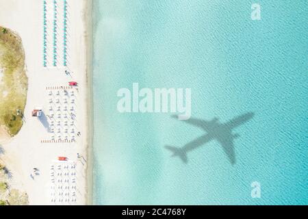 Vista dall'alto, splendida vista aerea di una spiaggia di sabbia bianca con ombrelloni e l'ombra di un aereo su un bellissimo mare turchese. Foto Stock