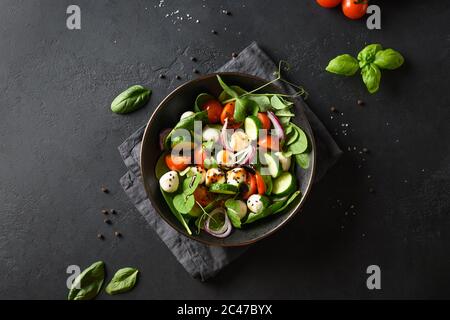 Insalata con spinaci, pomodori ciliegini, cipolla e mozzarella su fondo di pietra nera. Vista dall'alto. Foto Stock