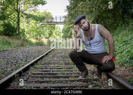 Giovane uomo francese con tatuaggi e macchie di carbone sulla pelle, portato fuori su una pista ferroviaria in disuso con luce naturale a Parigi, Francia Foto Stock