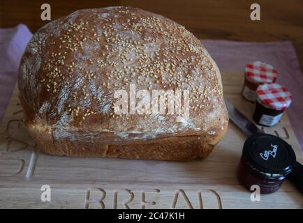 Pane bianco arricchito con uova fatte in casa con semi di sesamo su un pannello di legno con un coltello da pane e piccole pentole individuali di conserve Foto Stock