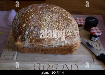 Pane bianco arricchito con uova fatte in casa con semi di sesamo su un pannello di legno con un coltello da pane e piccole pentole individuali di conserve Foto Stock