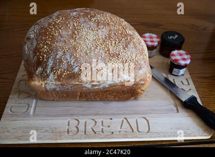 Pane bianco arricchito con uova fatte in casa con semi di sesamo su un pannello di legno con un coltello da pane e piccole pentole individuali di conserve Foto Stock