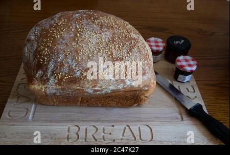 Pane bianco arricchito con uova fatte in casa con semi di sesamo su un pannello di legno con un coltello da pane e piccole pentole individuali di conserve Foto Stock