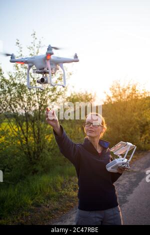 Bella, giovane donna che vola un quadricottero drone all'aperto, scattando foto aeree e riprese con esso Foto Stock