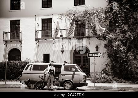 Vista posteriore dell'uomo più anziano che carica la bicicletta nel Vanagon Vintage Volkswagen, di fronte ad un edificio di stile spagnolo bello a Santa Barbara, CA, Stati Uniti, B&W Foto Stock