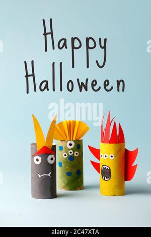 Happy HALLOWEEN testo, carta giocattolo fantasma, bat, mostri per Halloween party. Artigianato facile per i bambini su sfondo blu, idea creativa fai da te dal rotolo di carta igienata Foto Stock